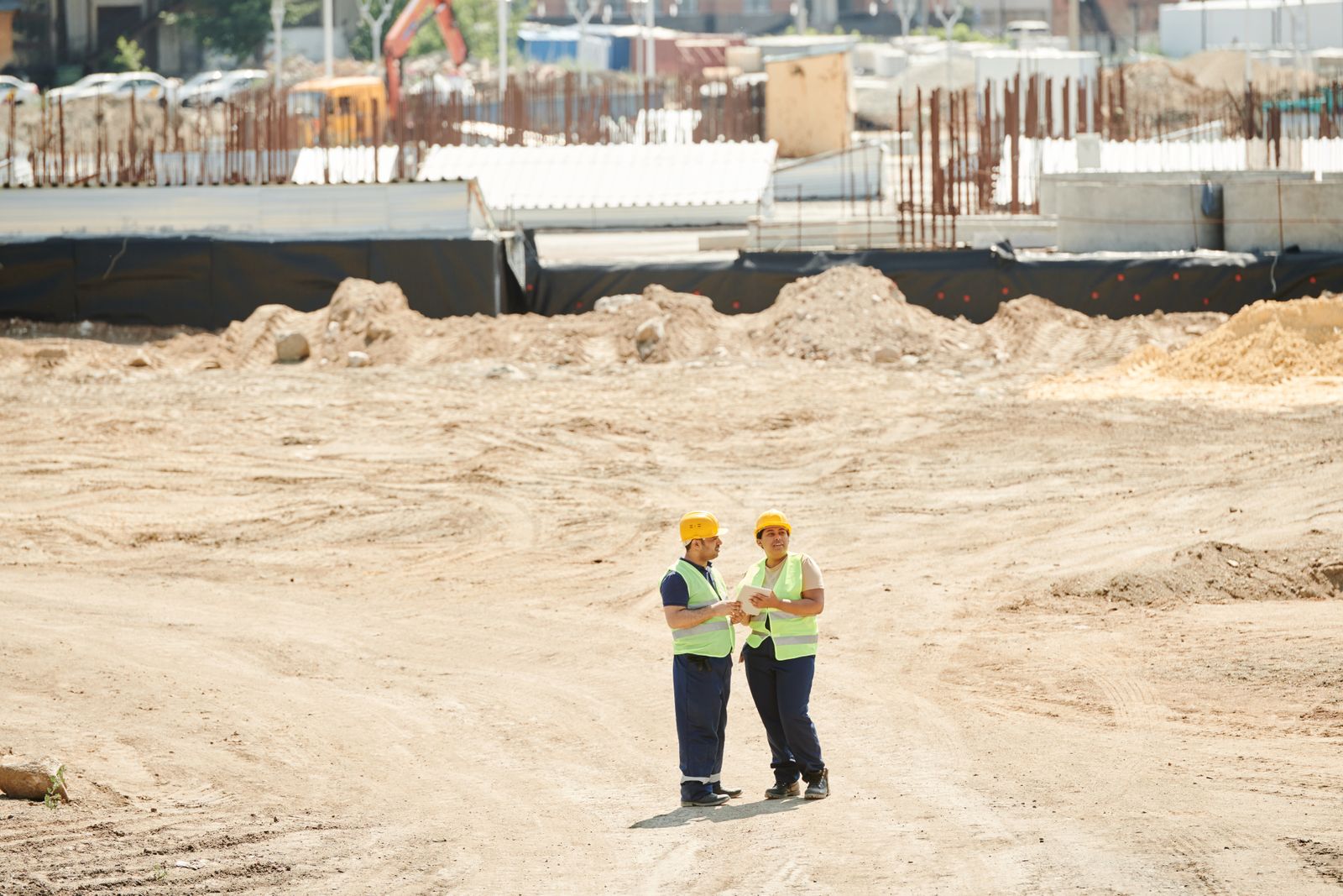 Two site workers in hard hats and hi-vis vests on a cleared construction site