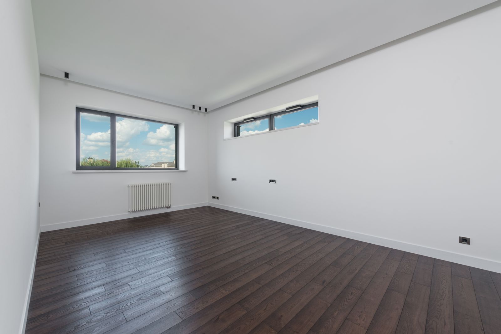 Newly finished empty room with white walls and dark wooden flooring