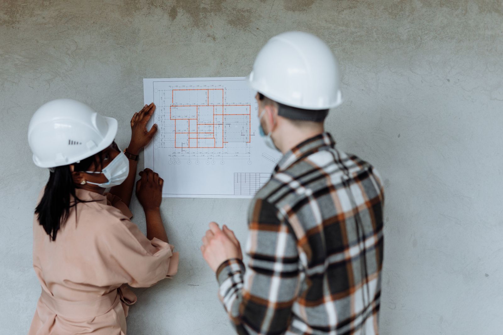 Two people in hard hats reviewing a floor plan on a concrete wall